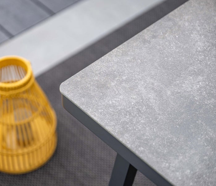 Nahaufnahme der Ecke eines Gartentisches mit Tischplatte in Steinoptik und Metallgestell.
