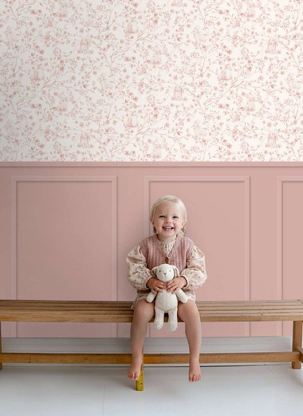 Kindersitzend auf einer Holzbank vor einer Wand mit Hasenmotiv-Tapete und Wandpaneelen im Kinderzimmer.