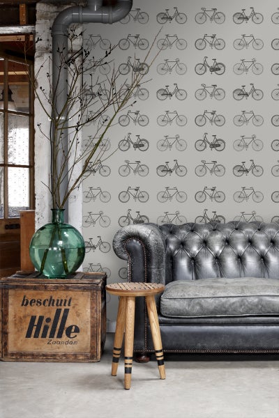 Wohnzimmer mit grauer Couch, Holzhocker und Tapete mit Fahrradmuster