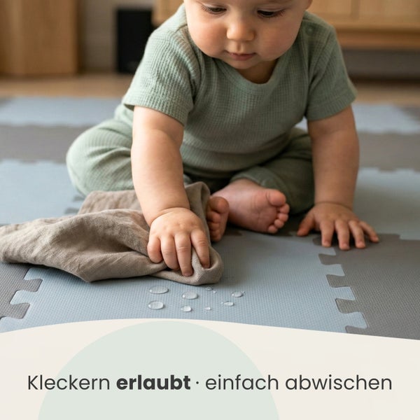 Baby wischt Wassertropfen auf einer Puzzle-Spielmatte mit einem Tuch ab, zeigt die abwischbare und wasserfeste Oberfläche.