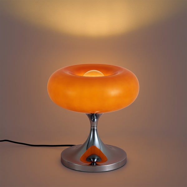 Moderne Tischleuchte mit ringförmigem Glasschirm und glänzendem Metallfuß, die warmes Licht verbreitet.