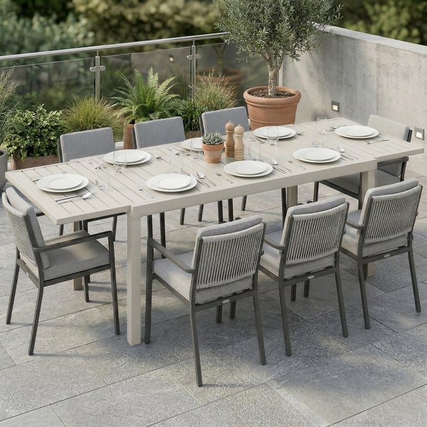 Moderne Garten-Essgruppe auf einer Terrasse, bestehend aus einem großen, hellen rechteckigen Lamellentisch und zehn passenden Stühlen mit Polstern.