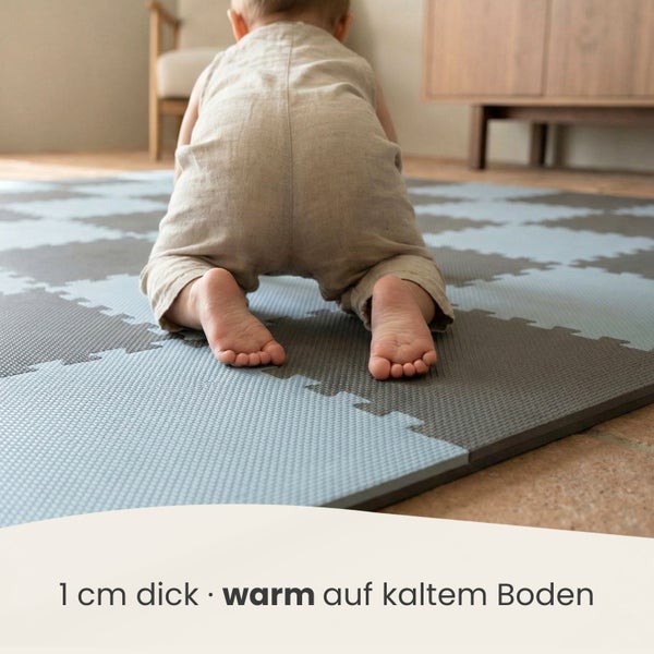 Baby krabbelt auf einer 1 Zentimeter dicken Puzzlematte aus Schaumstoff, die Wärme auf kaltem Boden bietet.