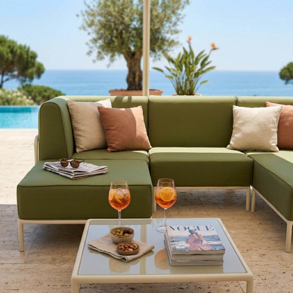 Modulares Garten Lounge Sofa mit grünen Polstern auf einer hellen Terrasse mit Pool und Meerblick, inklusive passendem Couchtisch und Kissen.