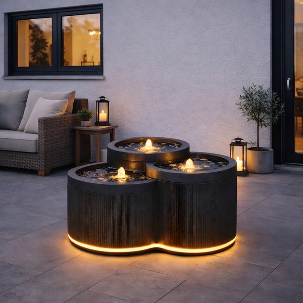 Dreistufiger Gartenbrunnen mit integrierter Beleuchtung auf einer Terrasse mit Loungemöbeln und Pflanzen.