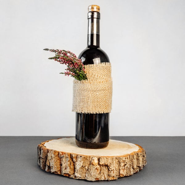 Dekorierte Flasche auf einer Baumscheibe, umwickelt mit Juteband und Heidekraut.