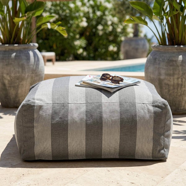 Gestreifter Outdoor-Sitzsack in einem hellen Gartenbereich mit Pool und großen Pflanzgefäßen aus Stein.