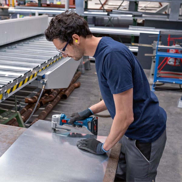 Ein Mann benutzt eine Akku-Blechschere von Bosch auf einer Metallplatte in einer Werkstatt.