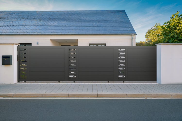 Modernes Schiebetor aus Aluminium in Anthrazit mit dekorativen Aussparungen vor einem hellen Wohnhaus.