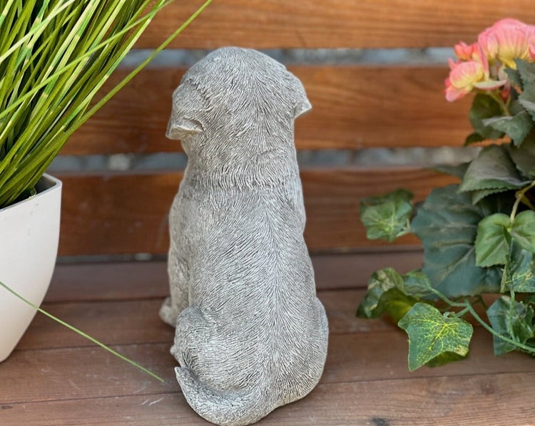 Gartenfigur Hund aus Steinguss, sitzend, von hinten fotografiert.