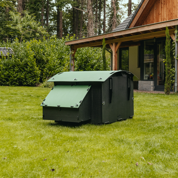 Moderner Hühnerstall aus recyceltem Kunststoff in einem hellen Garten auf einer Rasenfläche vor einem Haus mit Holzveranda.