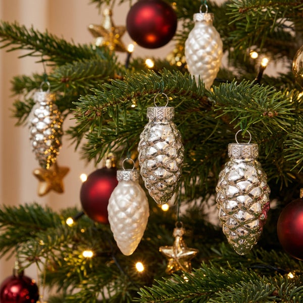 Weihnachtsbaum geschmückt mit Glasanhängern in Zapfenform, Kugeln und Sternen, ergänzt durch eine leuchtende Lichterkette.