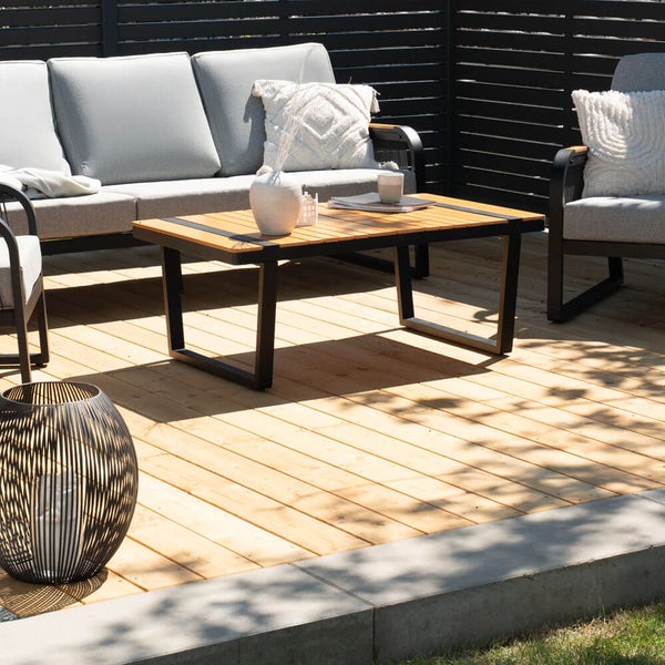 Gartenlounge Set mit Sofa und Tisch auf Holzterrasse mit Sichtschutz und dekorativen Kissen vor dem Hintergrund eines gepflegten Außenbereichs.