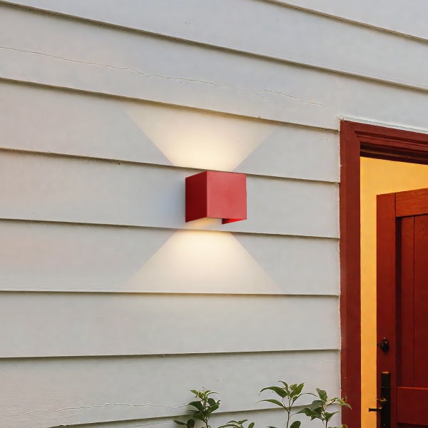 Rote würfelförmige Außenwandleuchte an einer weißen Holzfassade mit Lichtaustritt nach oben und unten.