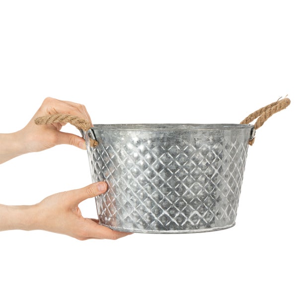 Pflanztopf aus verzinktem Metall mit geprägtem Rautenmuster und Seilgriffen, von zwei Händen gehalten.
