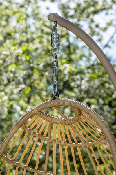 Detailaufnahme der Aufhängung eines beigefarbenen Hängesessels aus Geflecht mit Metallfeder und Kette an einem grauen Gestell.