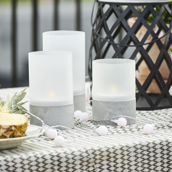 Dekorative Tischszene mit Windlichtern, Lichterkette und Ananas auf einer gemusterten Tischdecke.