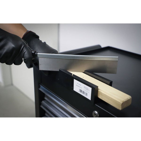Person mit schwarzen Schutzhandschuhen schneidet ein helles Holzstück in einer schwarzen Gehrungslade mit einer Feinsäge auf einem Werkstattwagen.