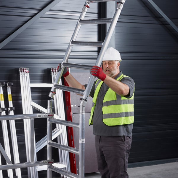 Ein Mann mit Schutzhelm und Sicherheitsweste montiert ein Gerüst.