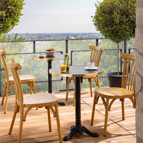 Balkon mit zwei runden Bistrotischen mit schwarzen Platten und Goldrand sowie vier hellen Holzstühlen auf einer Holzterrasse.