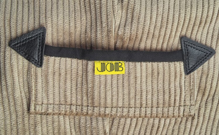Detailansicht von beigem Cordstoff mit schwarzem Tragegriff, Lumaland Logo und dreieckigen Lederverstärkungen.