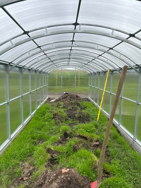 Innenansicht eines Gewächshauses mit Erde und Gartengeräten