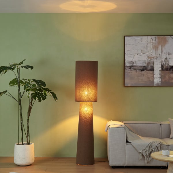 Moderne Stehlampe mit braunem Textilschirm in einem hellen Wohnzimmer mit Monstera-Pflanze, Stoffsofa und Wandbild.