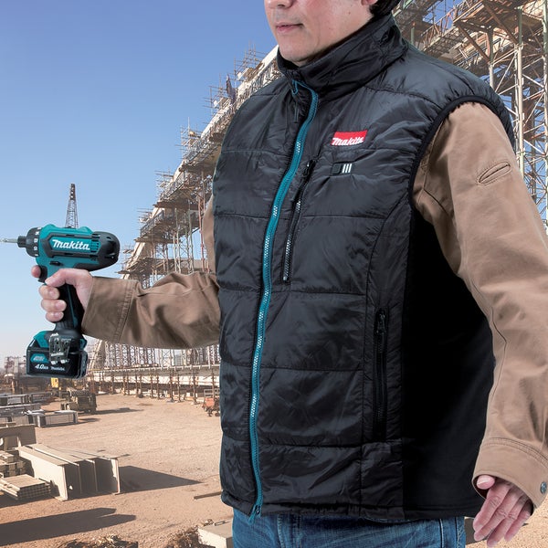 Ein Handwerker trägt eine beheizbare Makita Weste und hält einen Makita Akku Bohrhammer auf einer Baustelle.