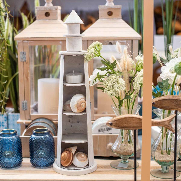 Dekorative Szene mit Leuchtturmregal, Windlichtern, Vasen, Blumen und maritimen Elementen für eine gemütliche Atmosphäre