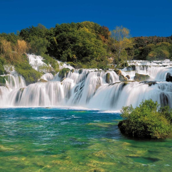 Wasserfall in grüner Landschaft unter blauem Himmel