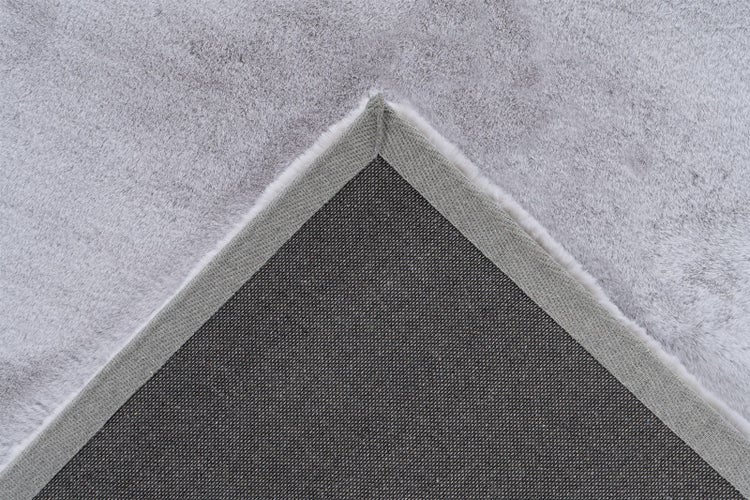 Detailansicht der Ecke eines grauen Teppichs mit weicher Oberseite und rutschhemmender Rückseite.