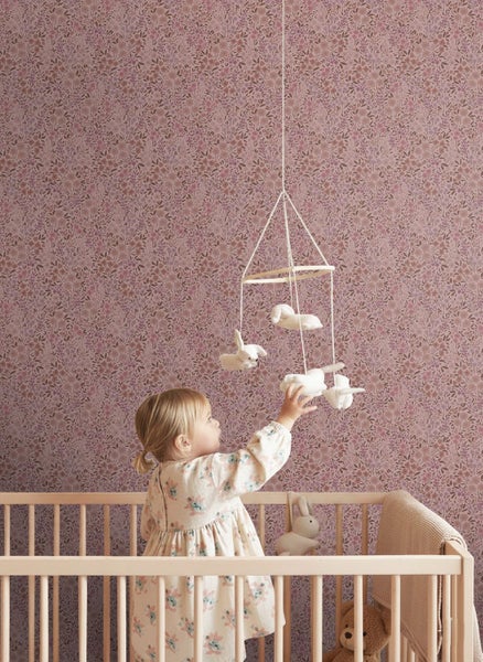 Vliestapete mit zartem Blumenmuster in einem Kinderzimmer mit Holzgitterbett und Mobile.