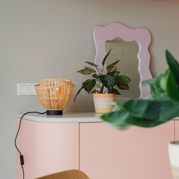 Dekorative Szene mit Tischleuchte aus Bambus, Zimmerpflanze und Spiegel auf einem Schrank