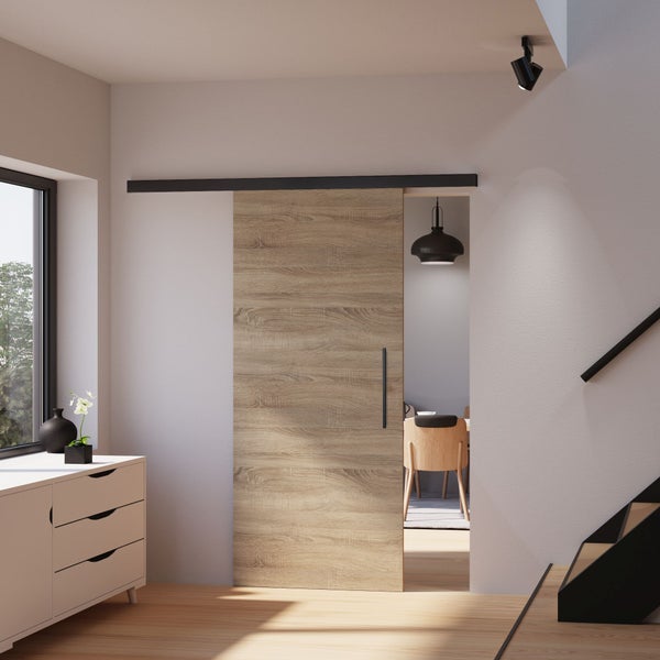 Moderne Schiebetür in Eiche-Optik mit schwarzer Laufschiene in einem hellen Wohnraum mit Treppe und Sideboard.