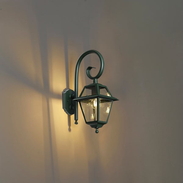 Klassische Außenwandleuchte im Laternen-Design mit geschwungenem Arm, Metallgehäuse und Glaseinsätzen, eingeschaltet.