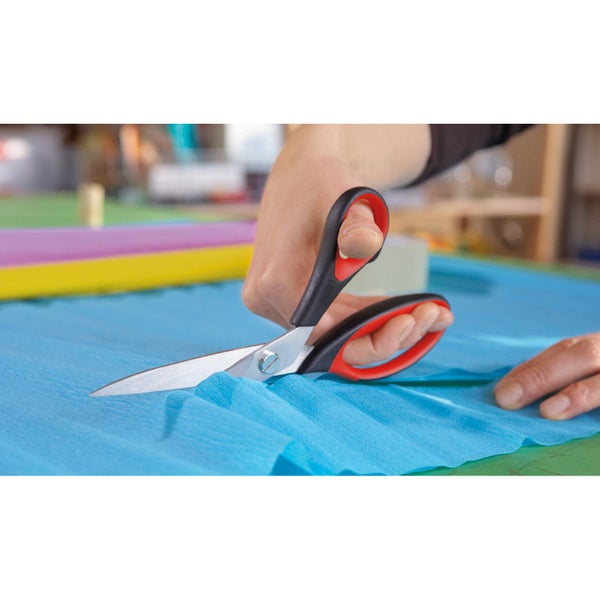 Eine Person schneidet mit einer Schere mit schwarz-roten Griffen blaues Krepppapier beim Basteln.