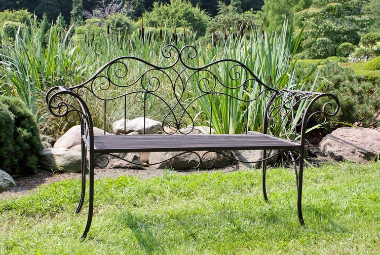 Gartenbank aus Metall mit verschnörkeltem Design an Rückenlehne und Armlehnen, auf einer Rasenfläche in einem hellen Garten.