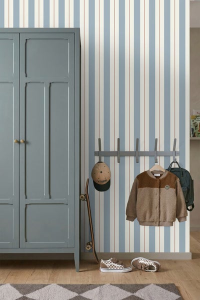 Gestreifte Vliestapete in Blau, Weiß und Terracotta in einem Kinderzimmer neben einem grauen Schrank und einer Garderobe.