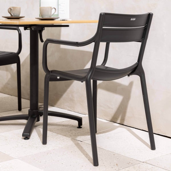 Moderner schwarzer Gartenstuhl aus Kunststoff mit Armlehnen an einem Holztisch mit Kaffeetassen in heller Umgebung.