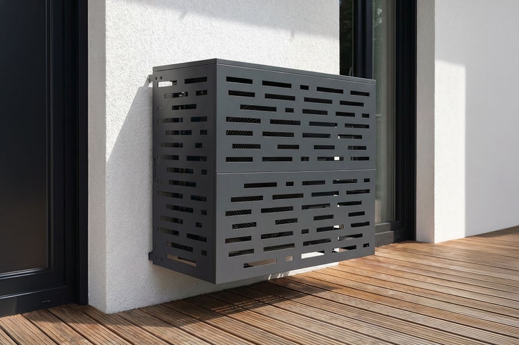 Wandmontierte Verkleidung für Klimaanlagen-Außengeräte mit Belüftungsschlitzen an einer Hauswand über einem Holzboden.