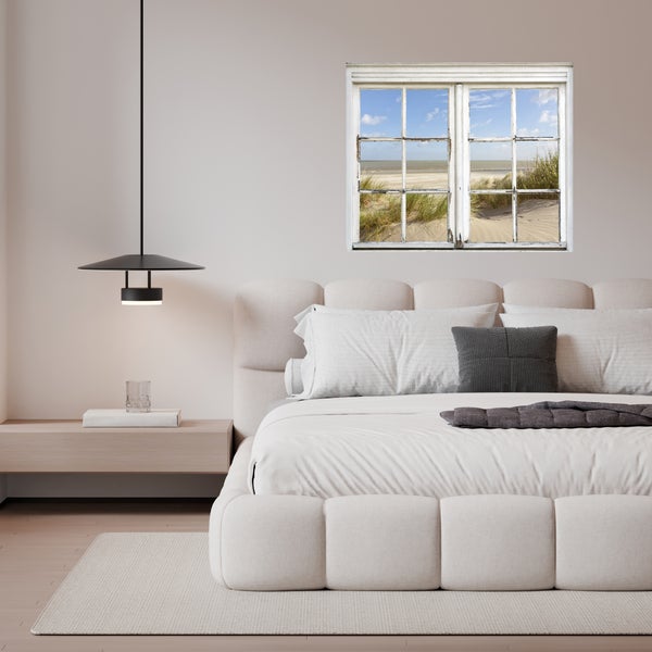 Schlafzimmer mit Bett, Nachttisch, Lampe und Fenster mit Blick auf den Strand