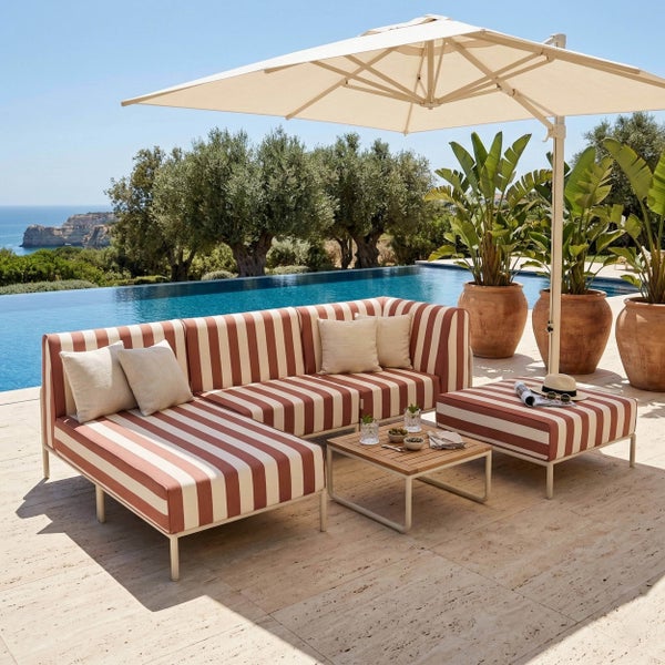 Moderne Gartenlounge mit rot und weiß gestreiftem Sofa, Hocker, Holztisch und Ampelschirm auf einer Terrasse mit Infinity-Pool und Meerblick.