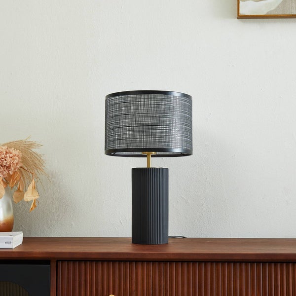 Dekorative Tischleuchte mit gemustertem Schirm und geriffeltem Sockel auf einem Holzschrank.