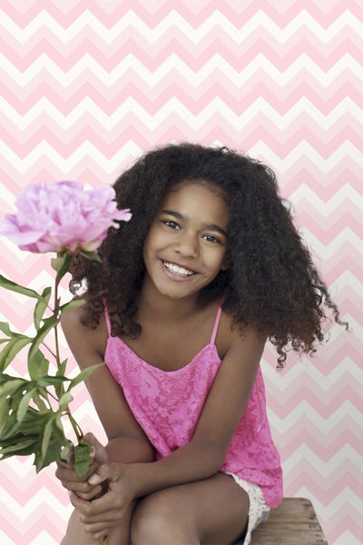 Lächelndes Mädchen mit Pfingstrose vor Zickzacktapete