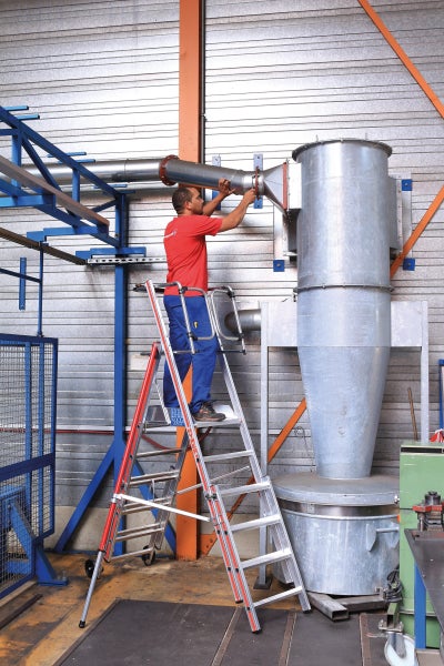 Mann arbeitet auf einer Mehrzweckleiter in einer Werkshalle an einem Rohr.
