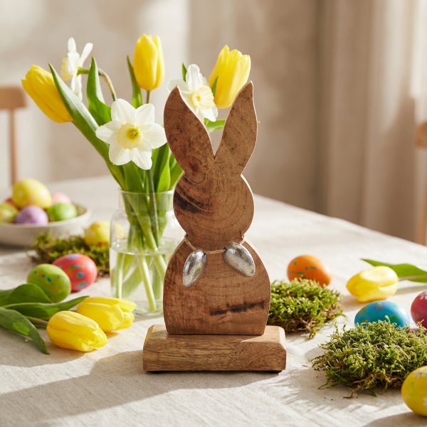 Osterdekoration aus Holz in Hasenform auf dem Tisch mit Blumen und bunt bemalten Ostereiern