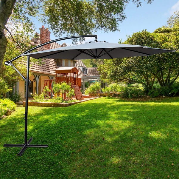 Freistehender Sonnenschirm im Garten mit Haus und Bäumen im Hintergrund.