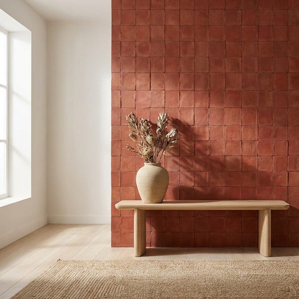 Wand mit quadratischen Fliesen in Ziegeloptik, davor eine Holzbank mit einer Vase aus Steingut und getrockneten Blumen in einem hellen Raum.