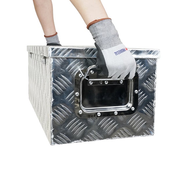 Person mit Arbeitshandschuhen greift an den seitlichen Tragegriff einer Aluminium-Transportbox mit Riffelblech-Oberfläche.