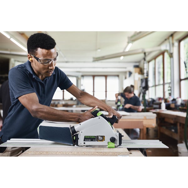 Handwerker nutzt eine Festool Akku-Tauchsäge mit Führungsschiene zum präzisen Schneiden einer Holzplatte in einer hellen Werkstatt.